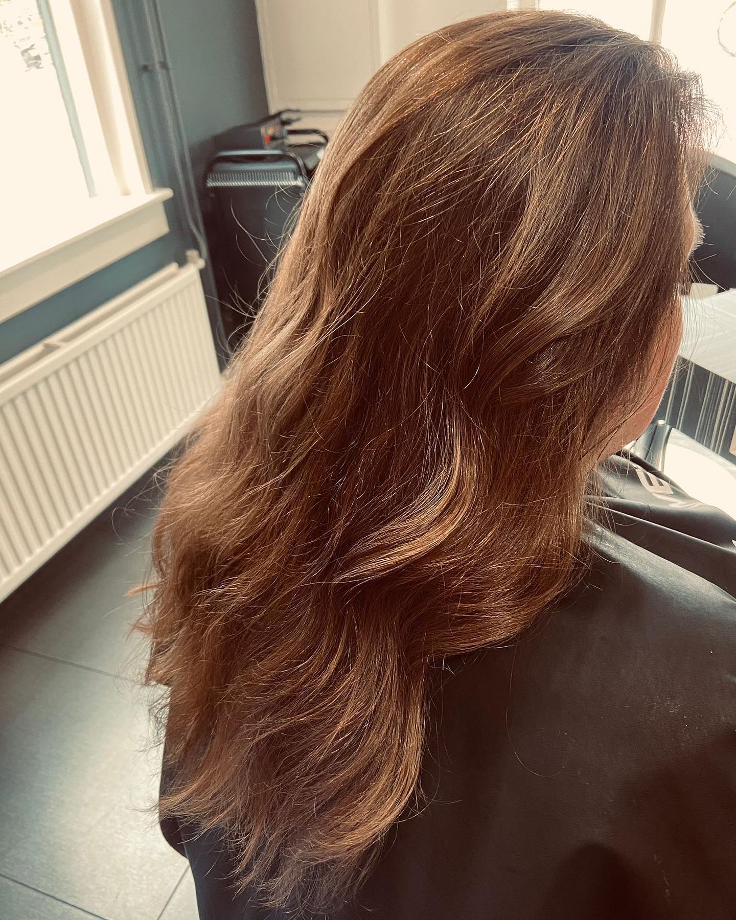 Kastanjebruin haar in laagjes geknipt, bij het raam van de salon